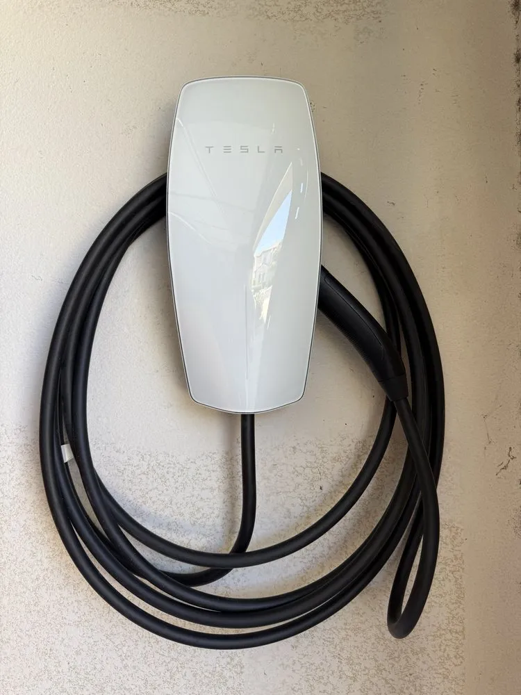 White Tesla Wall Connector mounted on a garage wall with its charging cable coiled beneath it.